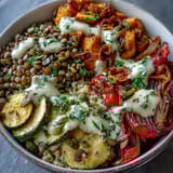A close-up of a vibrant Lentil Power Bowl with caramelized roasted vegetables and a drizzle of creamy tahini dressing over quinoa.  