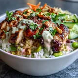 Creamy coconut rice topped with tender grilled chicken and fresh vegetables, drizzled with rich peanut sauce for a nourishing bowl meal.  
