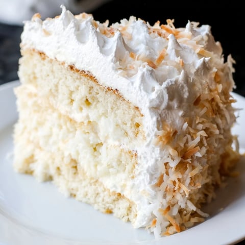 A majestic Coconut Cake, layered with creamy coconut filling and fluffy seven-minute frosting, ready to be enjoyed.