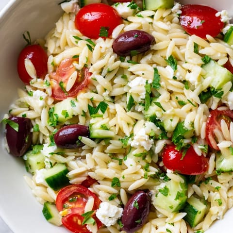 A vibrant bowl of Greek Orzo Salad with cherry tomatoes, cucumber, and crumbled feta tossed in a bright lemon-oregano dressing.