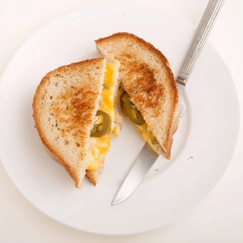 Golden-brown Cheddar Jalapeño Grilled Cheese on a white plate beside creamy tomato soup, perfect for a cozy weeknight dinner.