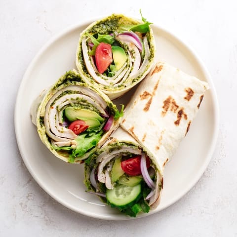 Bright green herb sauce coats sliced grilled chicken inside this colorful Chimichurri Chicken Salad Wrap on a wooden table.  