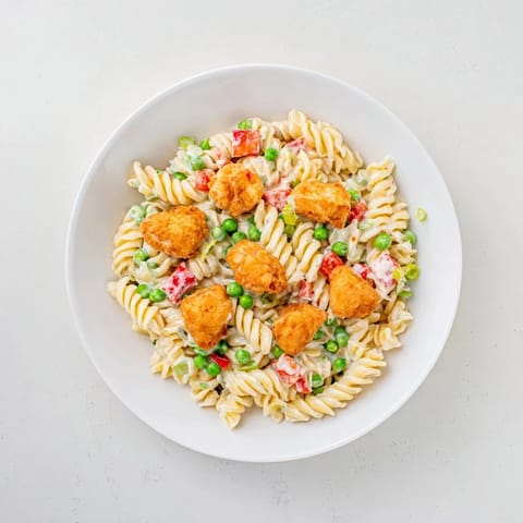 Golden panko-crusted chicken pieces rest atop a colorful bowl of Crispy Chicken Ranch Pasta Salad with peas and red bell pepper. 