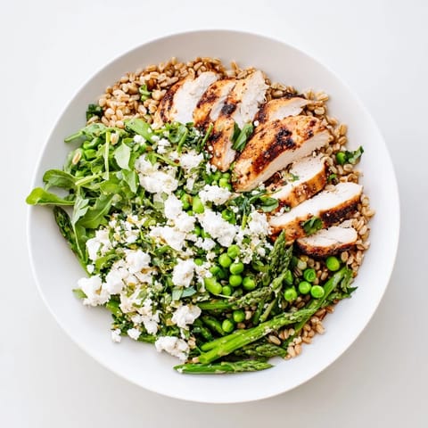 A hearty serving of warm spring farro chicken salad topped with crumbled feta, fresh herbs, and zesty lemon on a white plate, ready for lunch.  
