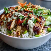 Creamy coconut rice topped with tender grilled chicken and fresh vegetables, drizzled with rich peanut sauce for a nourishing bowl meal.  